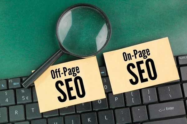 A magnifying glass rests on a laptop keyboard next to two sticky notes labeled "Off-Page SEO" and "On-Page SEO," highlighting key aspects of search engine optimization.